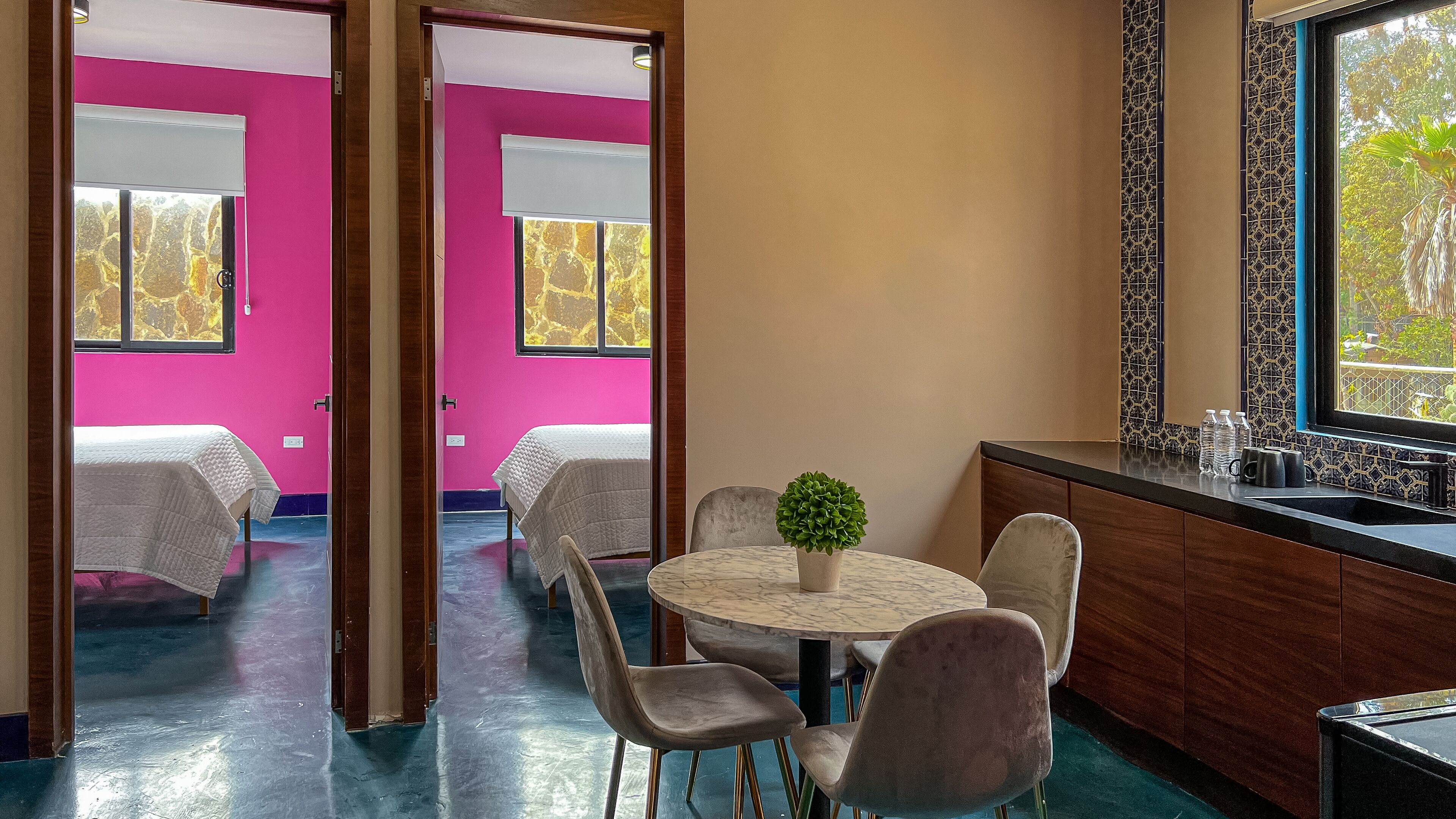 Une pièce avec une table ronde, quatre chaises, une plante en pot et une fenêtre donnant sur des arbres.