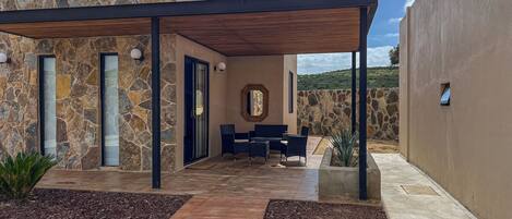 A modern outdoor patio with stone walls, a wooden pergola, and a seating area with chairs and a table.
