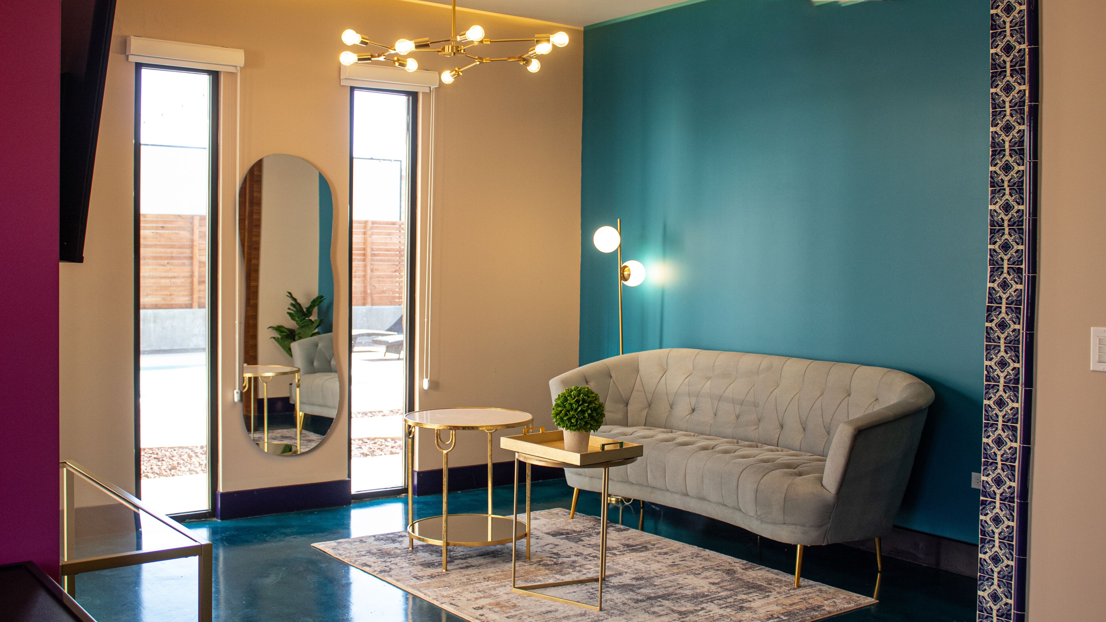 A modern living room with a tufted sofa, a round coffee table, a small side table, a mirror, and a chandelier.