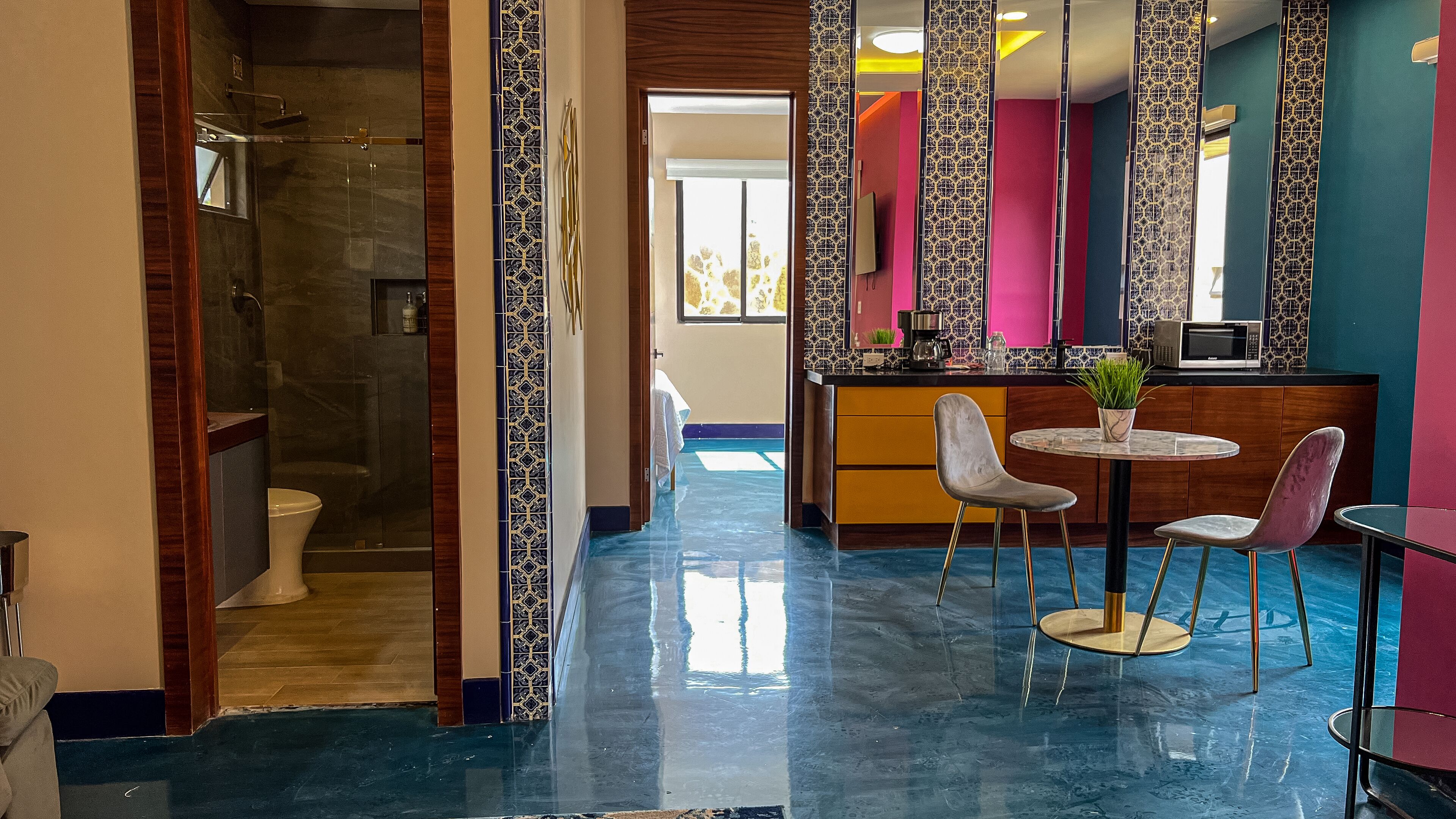 Um hall de hotel com chuveiro em cabine de vidro, balcão de recepção e área de estar com duas cadeiras e uma mesa.