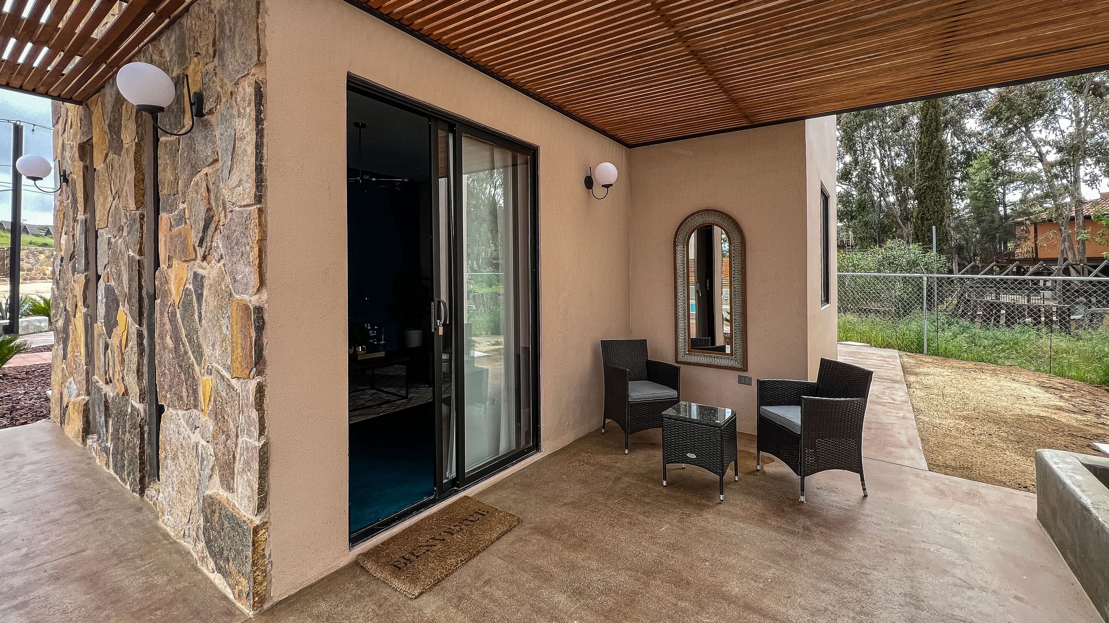 A covered patio with stone walls, a sliding glass door leading to an outdoor area, and wicker furniture.