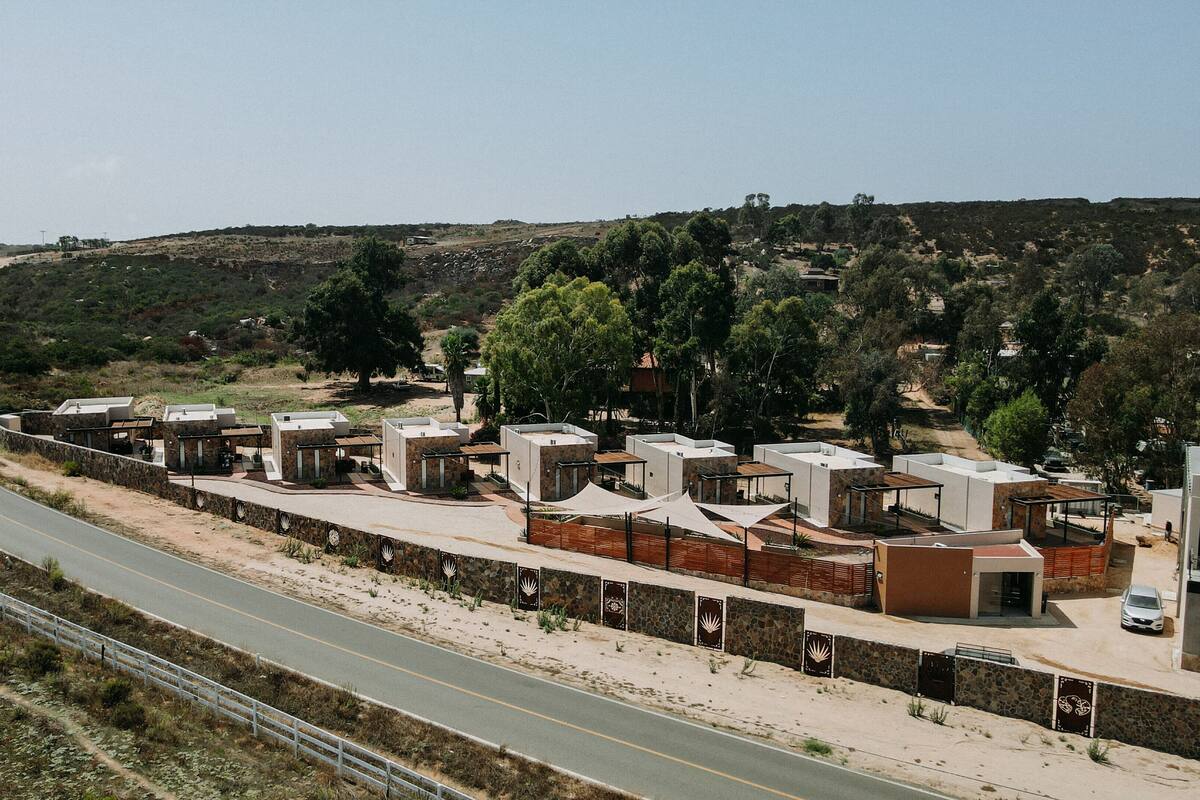 A coastal road with a row of modern, compact buildings with flat roofs, likely a hotel or resort, adjacent to the road.
