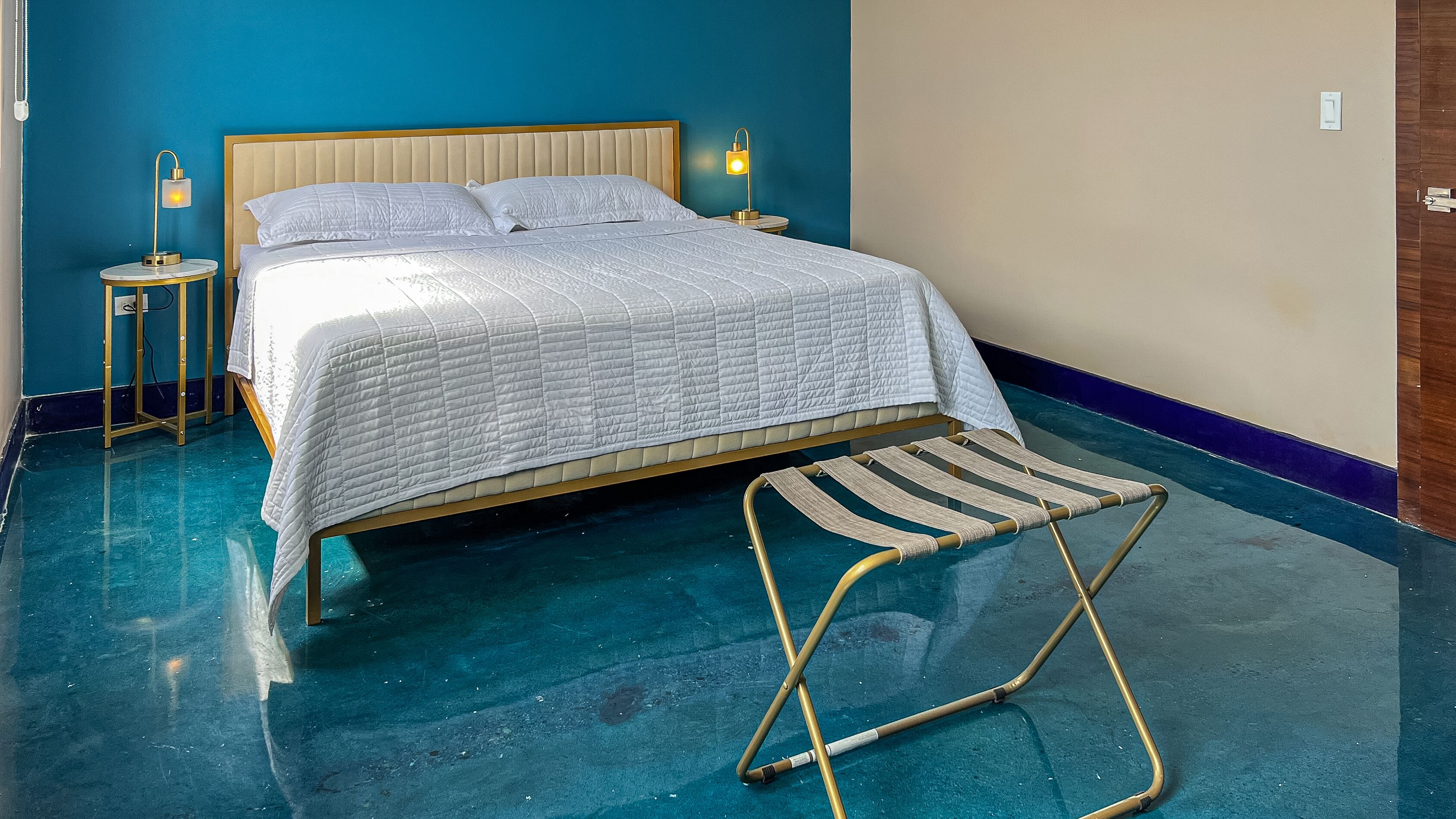 Quarto com cama, duas luminárias de cabeceira e um banquinho.