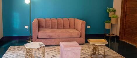 Une pièce avec un mur de couleur turquoise, un canapé rose, une table basse en marbre et deux tables d’appoint à cadre doré.