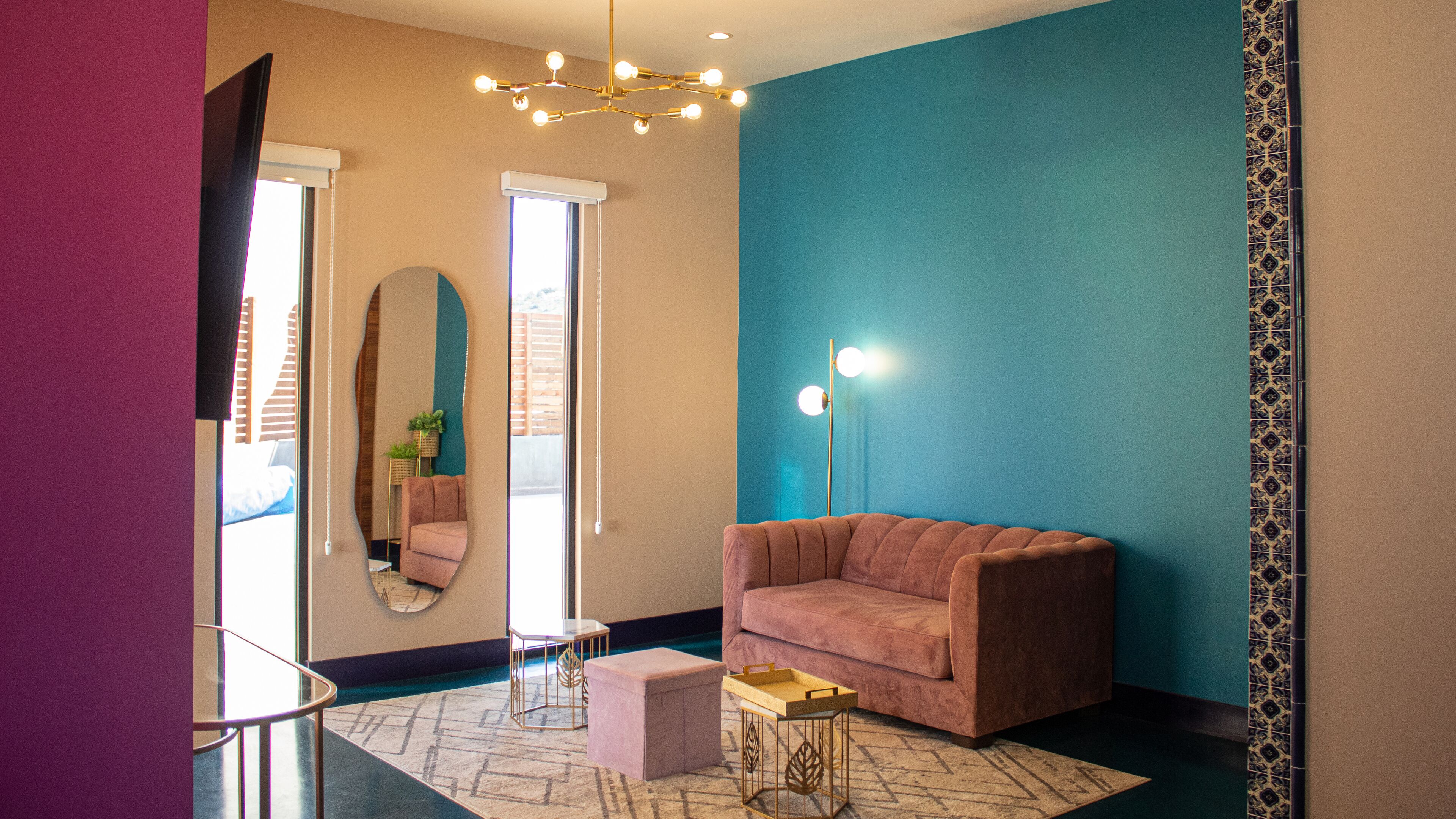 A modern living room with a pink sofa, a round mirror, a floor lamp, and a small table.