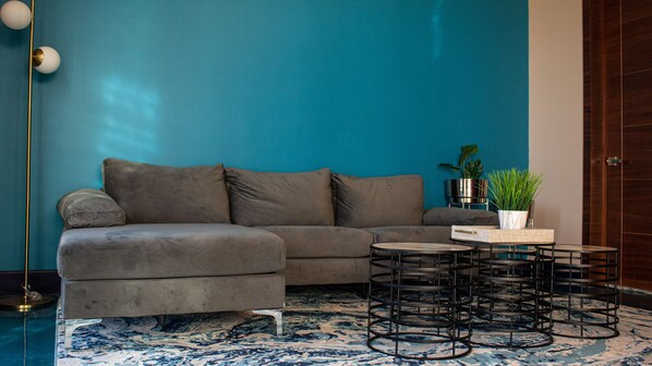 A modern living room with a grey sectional sofa, a round coffee table with metal legs, and a blue patterned rug. - Catrina (Valle de Guadalupe)