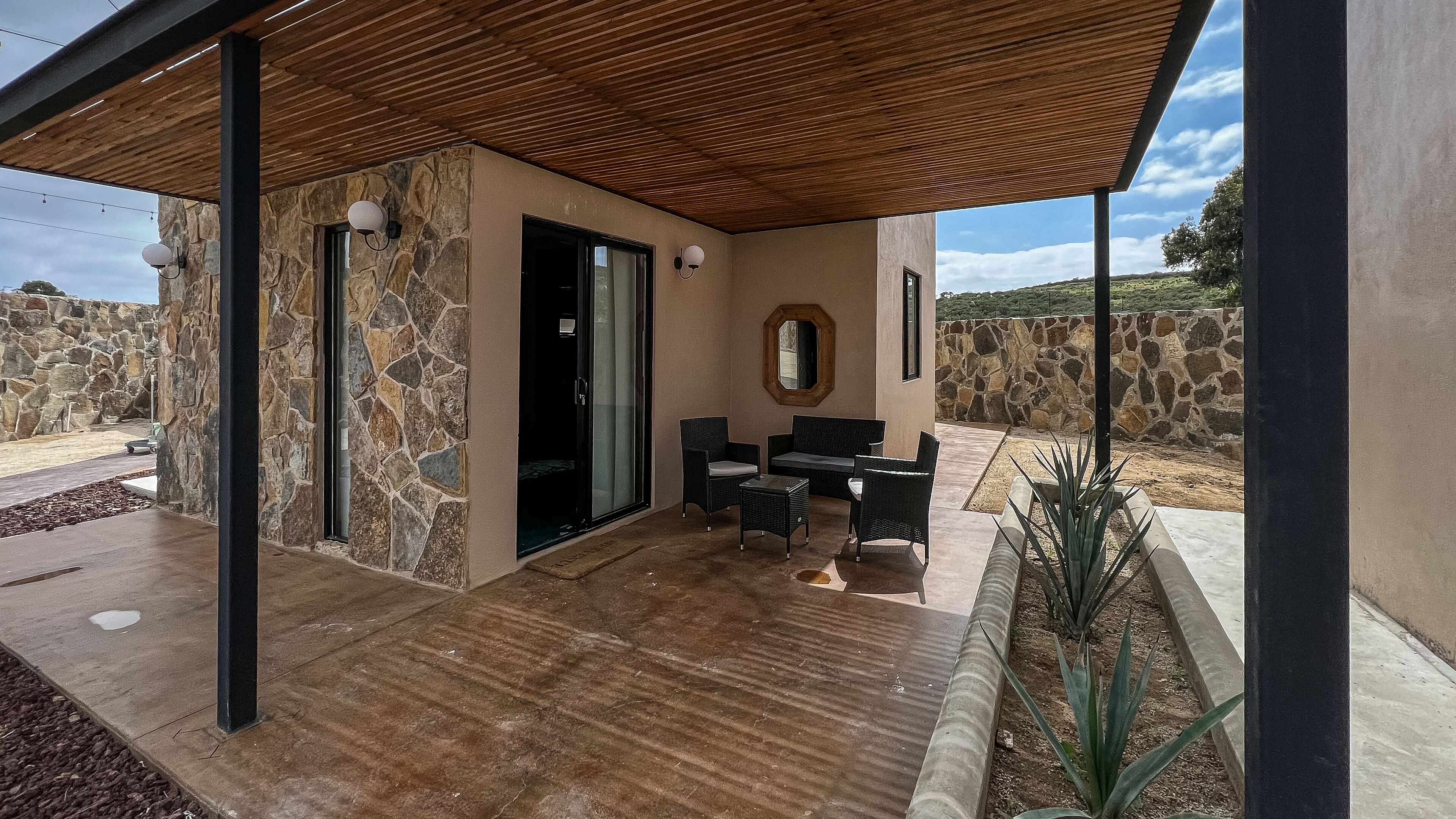 A covered outdoor seating area with stone walls, a wooden ceiling, and a view of the landscape.