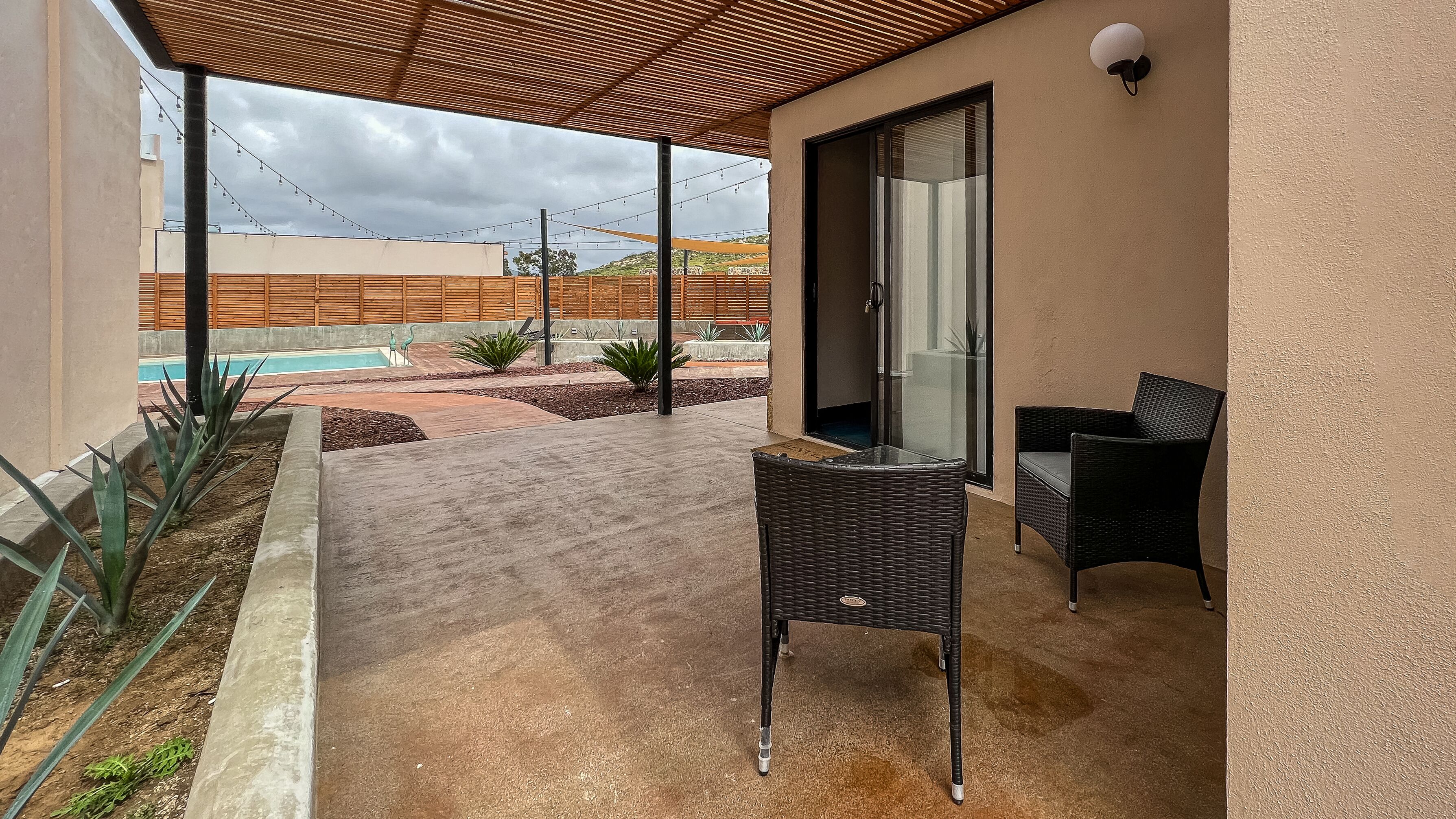 Un espacio al aire libre techado con piscina, dos sillas de mimbre y una pérgola.