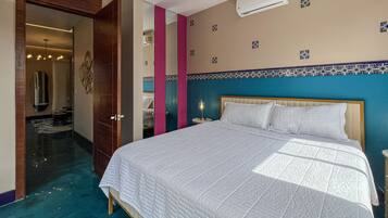 A hotel room with a large bed, a nightstand, a mirror, and a bathroom visible through an open door.