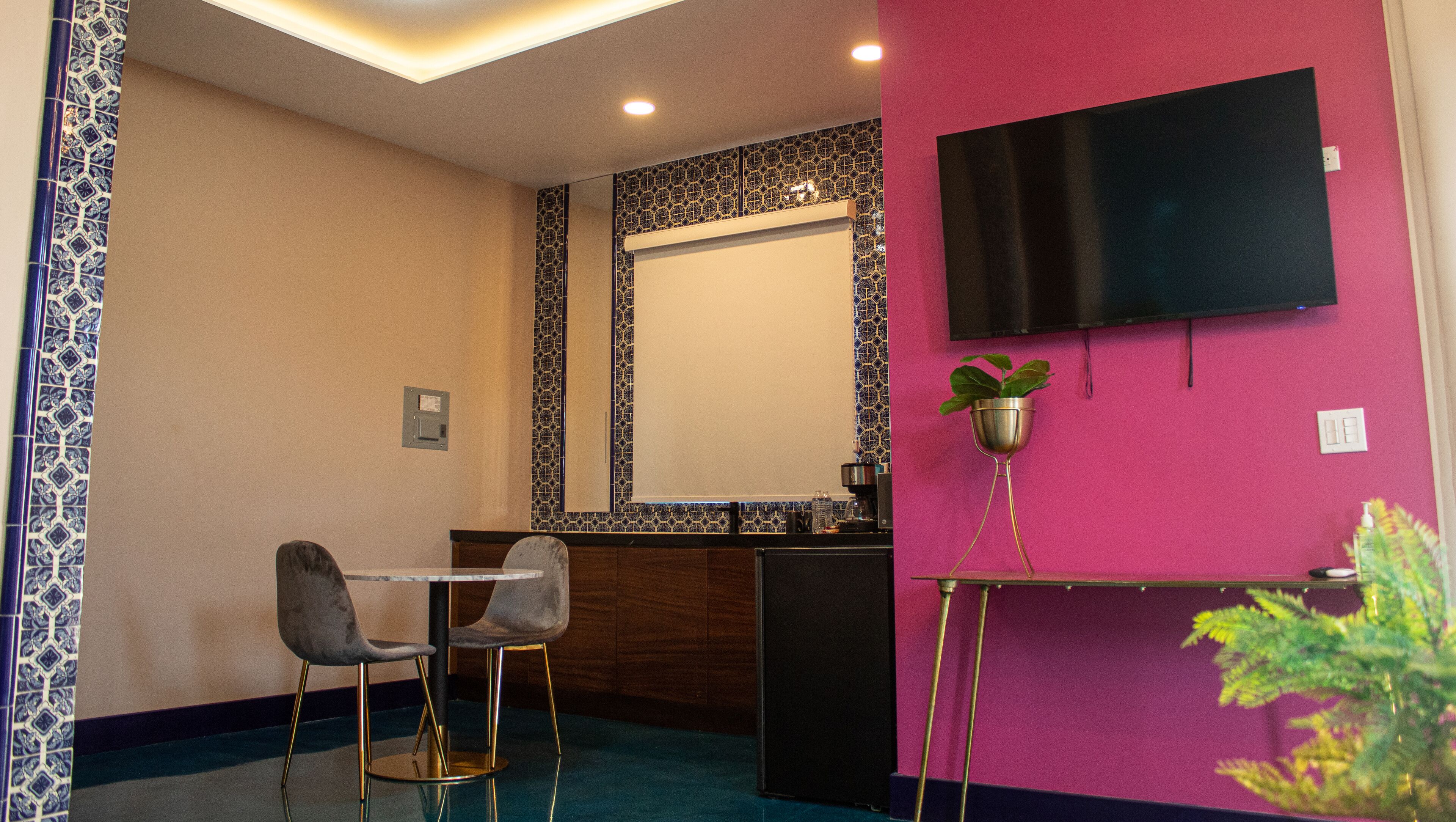 Habitación de hotel con comedor, televisor montado en la pared y una planta en maceta.