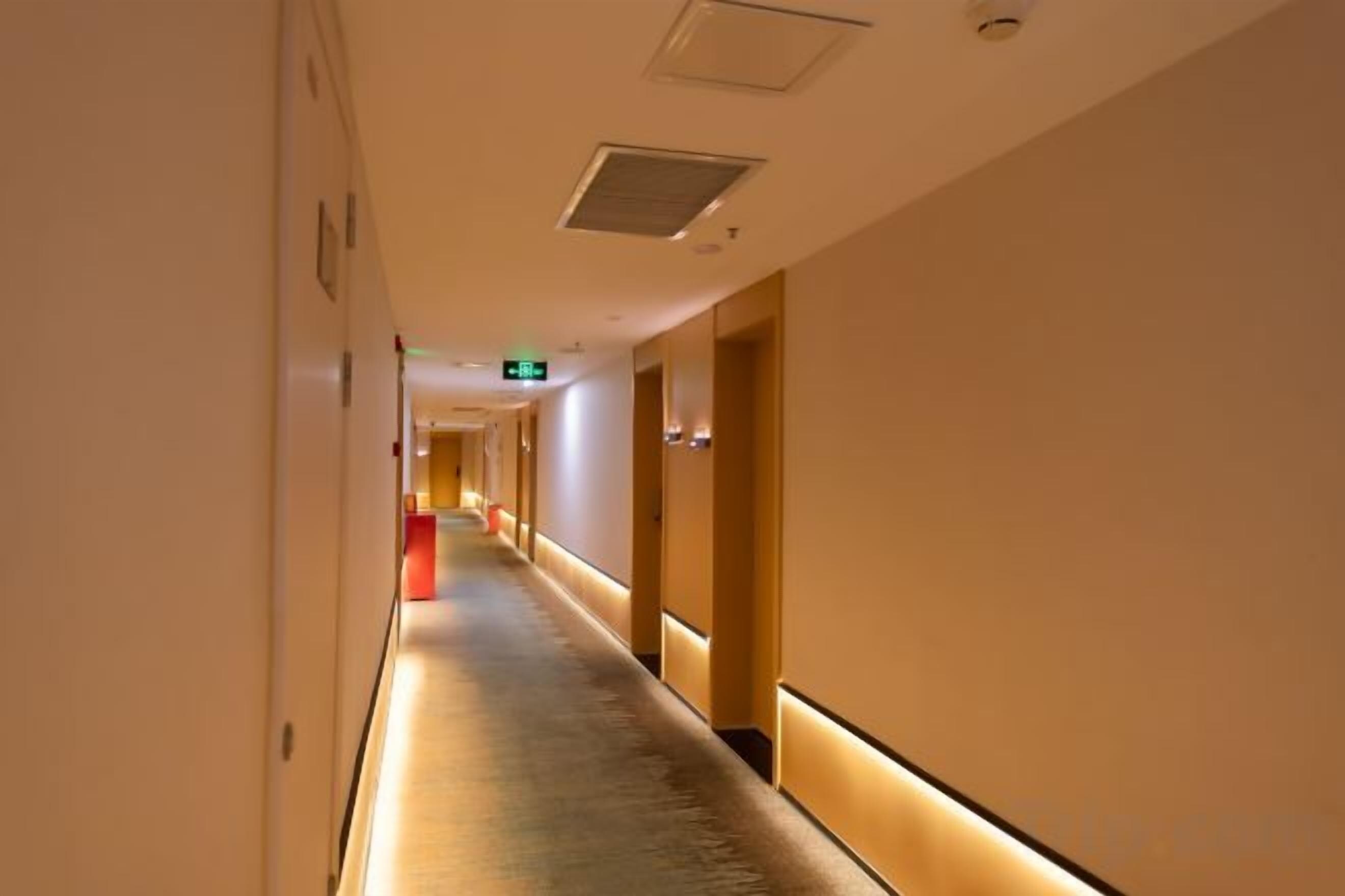 A hotel corridor with a carpeted floor, doors on both sides, and a light fixture on the ceiling.