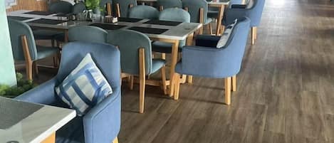 Un restaurante con mesas y sillas dispuestas en filas, suelo de madera y vista a la calle.