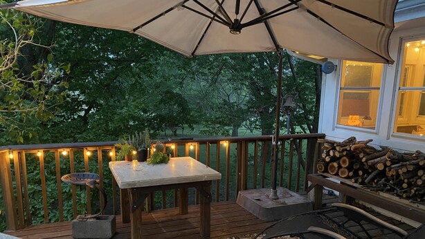 Een houten terras met een tafel en stoelen, een grote parasol en uitzicht op bomen.