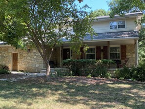 A two-story house with a stone facade, a covered porch, and a tree in the foreground.