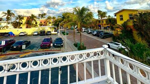 A balcony with a white railing overlooking a parking lot with several cars, palm trees, and buildings in the background. - Pousada Suites at Hollywood Beach (Hollywood)