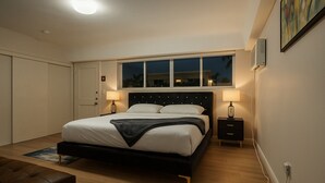 A bedroom with a bed, bedside tables, a nightstand, a lamp, a window, and a door. - Pousada Suites at Hollywood Beach (Hollywood)