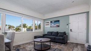 A living room with a sofa, a coffee table, and a view of palm trees through large windows. - Pousada Suites at Hollywood Beach (Hollywood)