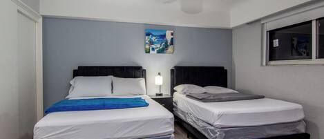 A hotel room with two beds, a ceiling fan, a nightstand with a lamp, and a painting on the wall.