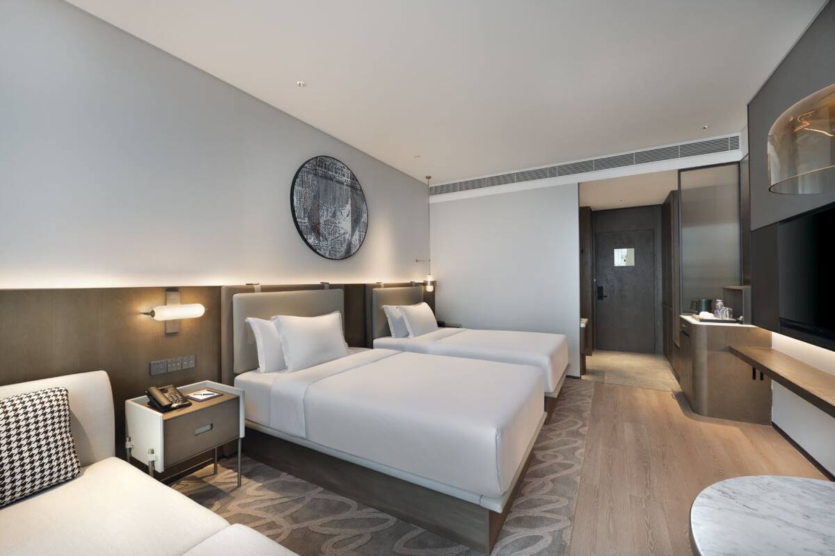 Een moderne hotelkamer met twee bedden, een bureau, een stoel, een televisie en een groot kunstwerk aan de muur.