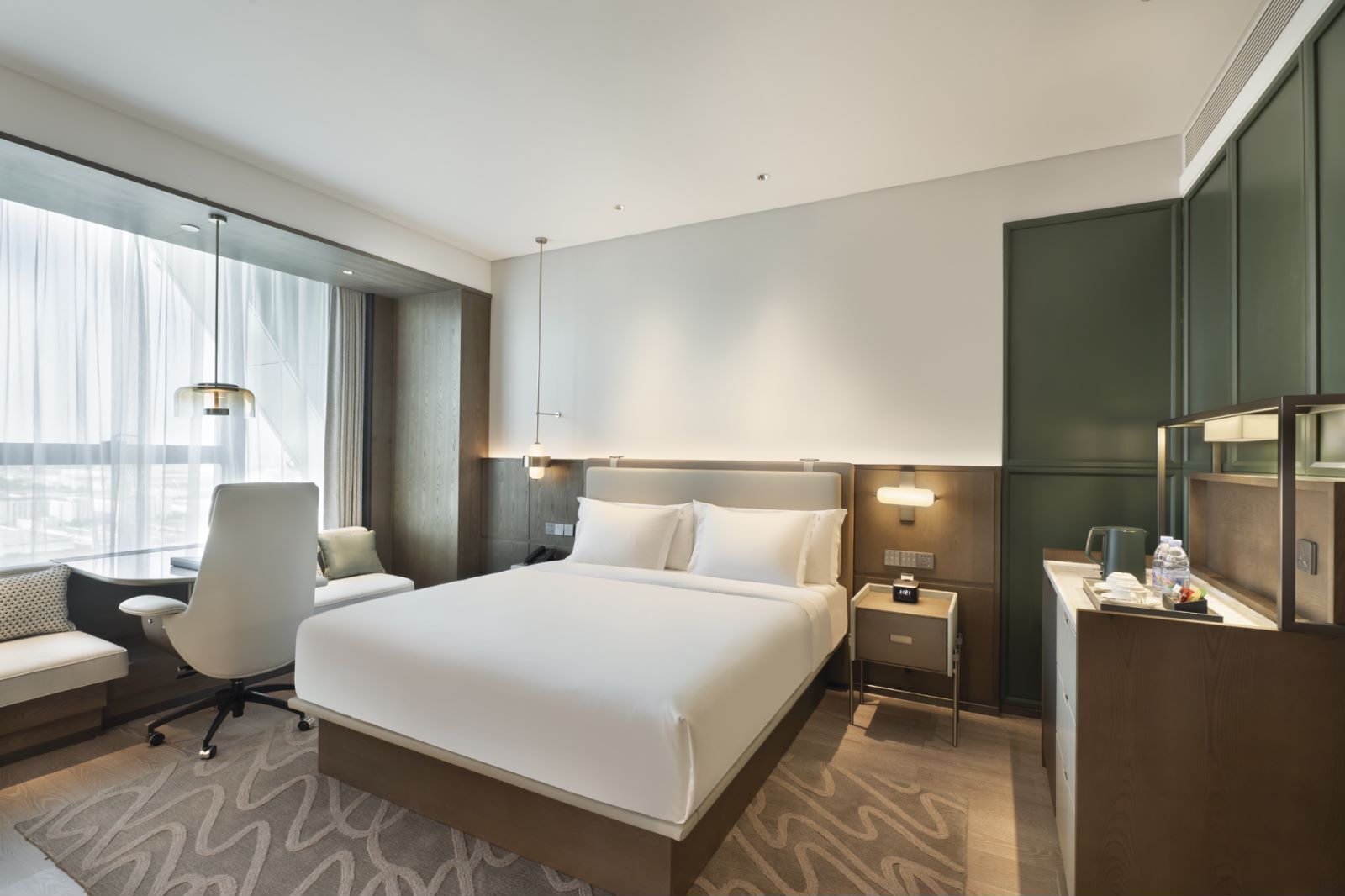 A modern hotel room with a large bed, a desk, a chair, a nightstand, and a mirror.