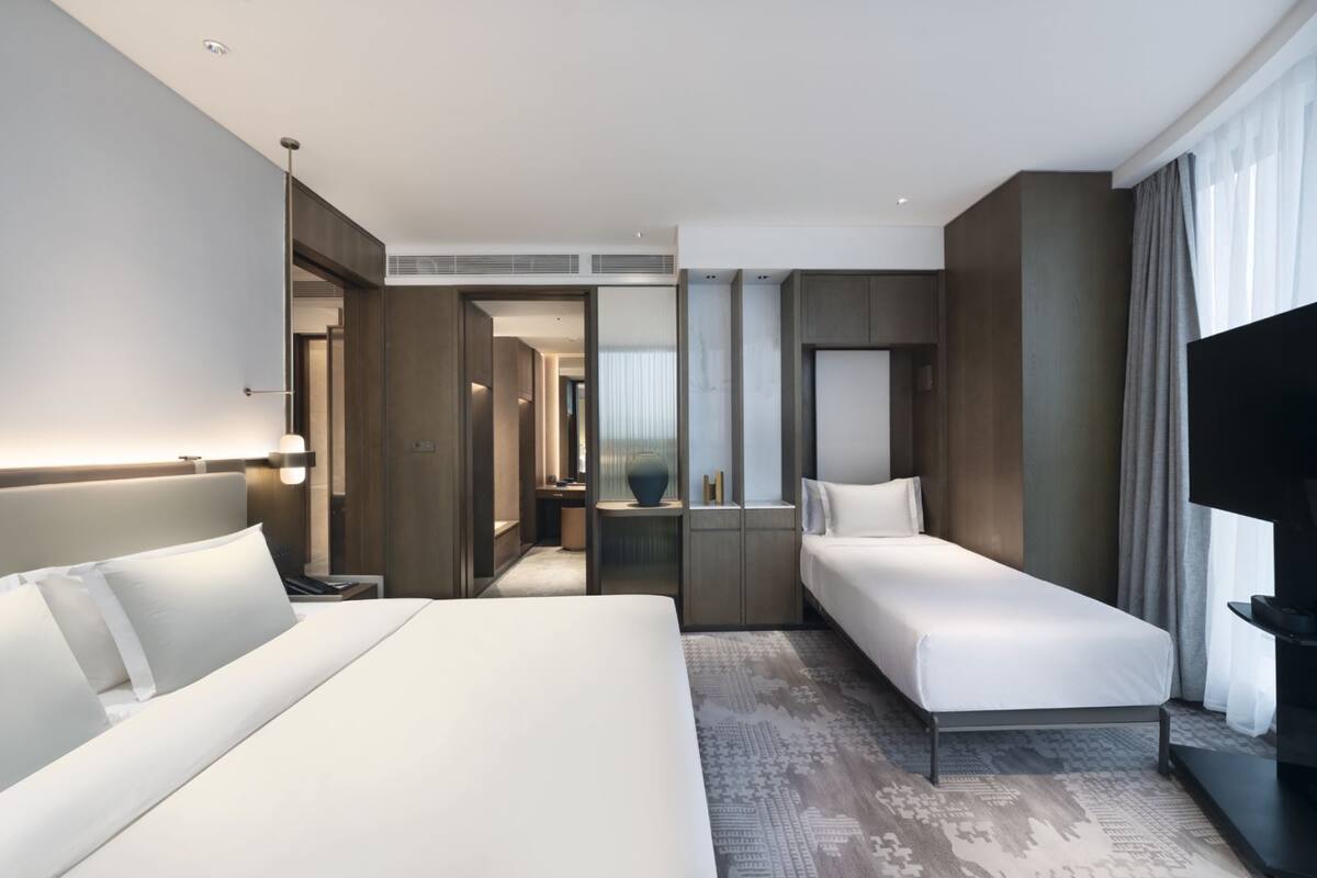Een moderne hotelkamer met een groot bed, een kleiner bed, een televisie en een inloopkast.
