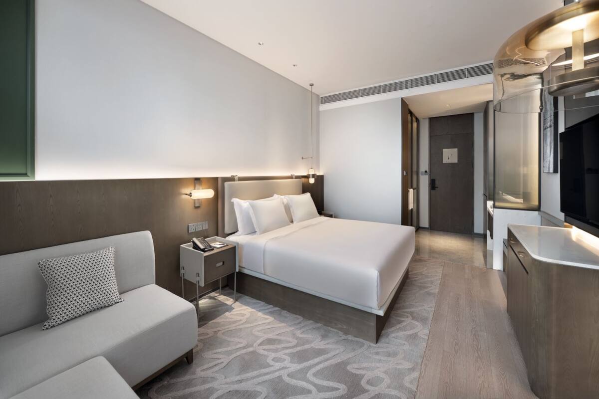 Een moderne hotelkamer met een bed, een slaapbank, een nachtkastje en een badkamer, zichtbaar door een open deur.