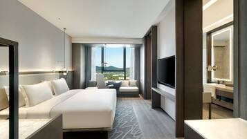 A modern hotel room with a large bed, a TV, a desk, and a bathroom with a mirror.