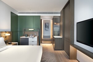 Una habitación de hotel moderna con una cama grande, un escritorio con silla, un televisor de pantalla plana y un baño con ducha e inodoro.