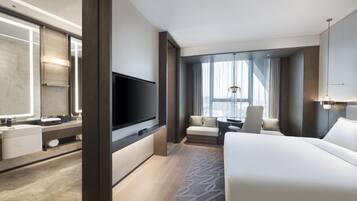 A modern hotel room with a large bed, a flat-screen TV, a sofa, and a desk.