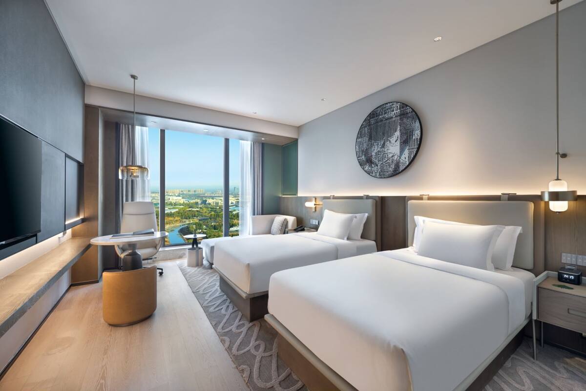 Een moderne hotelkamer met twee bedden, een zithoek en een groot raam met uitzicht op de stad.