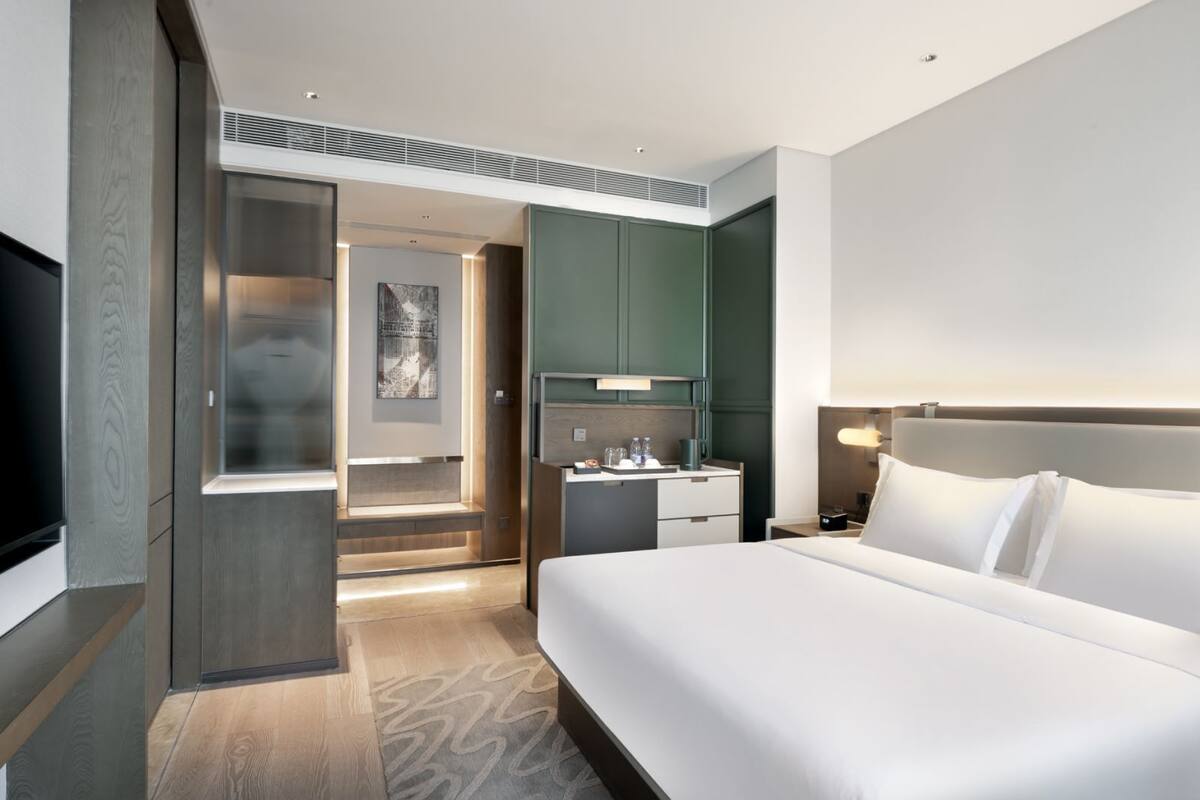 Een moderne hotelkamer met een groot bed, een televisie, een bureau met stoel, en een badkamer met spiegel en wastafel.