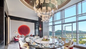 Un espace repas moderne avec une table ronde dressée pour six personnes, entourée de chaises à revêtement rouge. Un grand élément décoratif circulaire rouge orne le mur derrière les sièges.