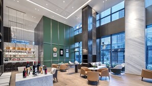 Un hall d’hôtel moderne doté d’un bar, de différents espaces de détente et de grandes fenêtres offrant une vue sur la ville.
