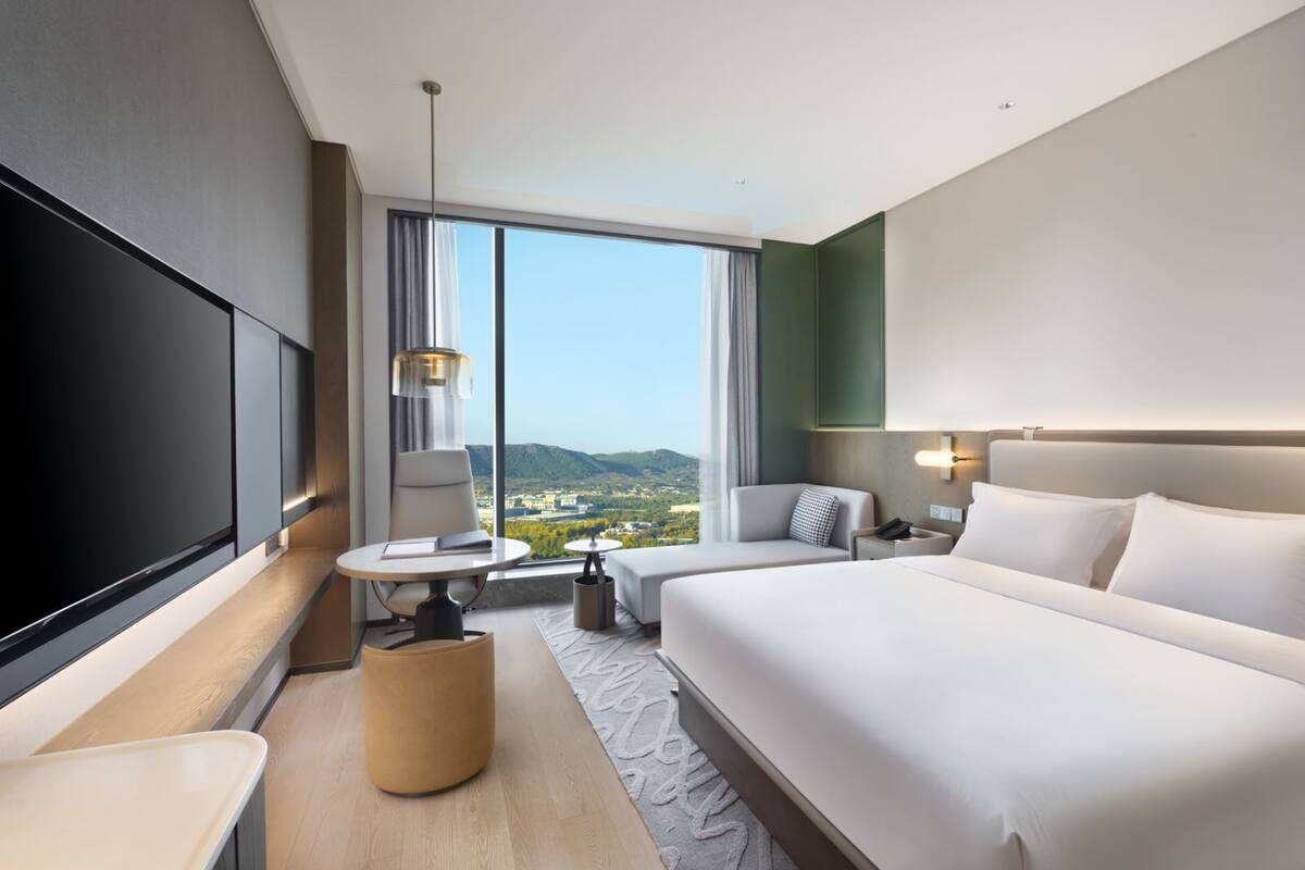 Een moderne hotelkamer met een groot bed, een bureau, een stoel, een televisie en uitzicht op de stad en de bergen.