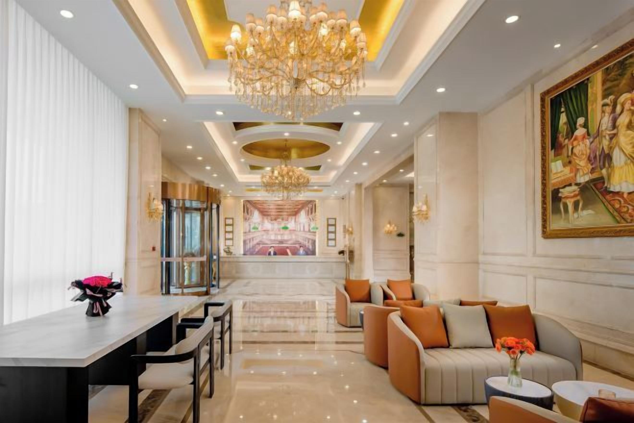 A hotel lobby with a chandelier, seating area, and a painting on the wall.