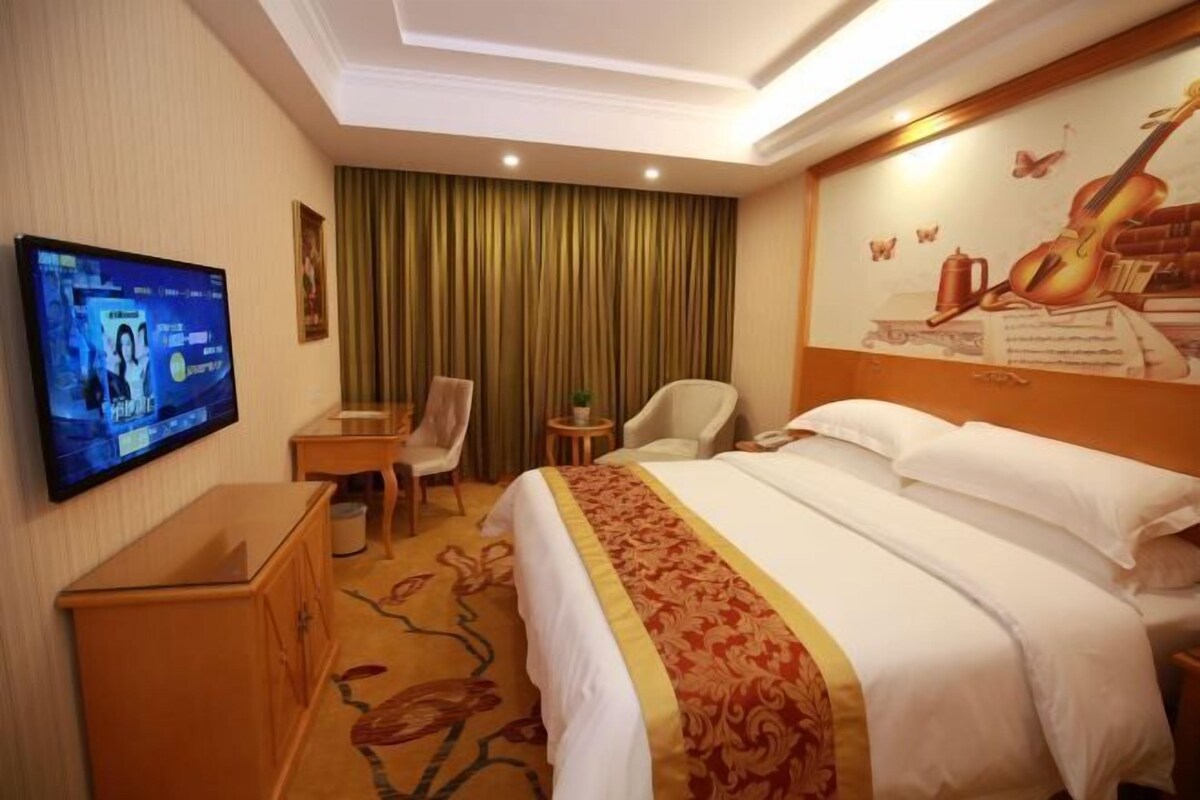 A hotel room with a bed, a television, a desk, a chair, and a curtain.