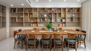 A dining area with a long wooden table surrounded by chairs, a bookshelf filled with books, and a potted plant on the table. - Vienna Hotel (Liuyang Xincheng International) (Liuyang)