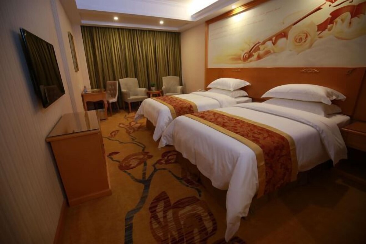 A hotel room with two beds, a television, a desk, and a chair.