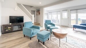 A spacious living room with a staircase, a television, and blue furniture. - 80 Feet of Private Lakefront House (Amherstburg)