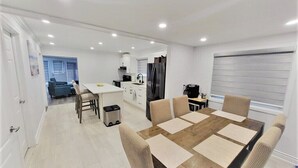 A modern kitchen with white cabinets, a black refrigerator, and a coffee machine. There is a dining area with a wooden table and beige chairs. - 80 Feet of Private Lakefront House (Amherstburg)