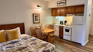 A compact room with a bed, a dining table with chairs, a kitchenette with a refrigerator and stove, wooden cabinets, and a framed picture on the wall. - Cozy King Bed Studio - Mtn Views - Direct River Access in back (Lincoln)
