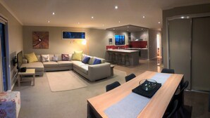 Ein modernes Wohnzimmer mit einer Couch, einem Esstisch und einer Küchenzeile im Hintergrund.