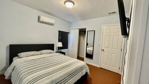 Ein Schlafzimmer mit einem Bett, einem Nachttisch, einem Spiegel, einer Tür und einer Klimaanlage.