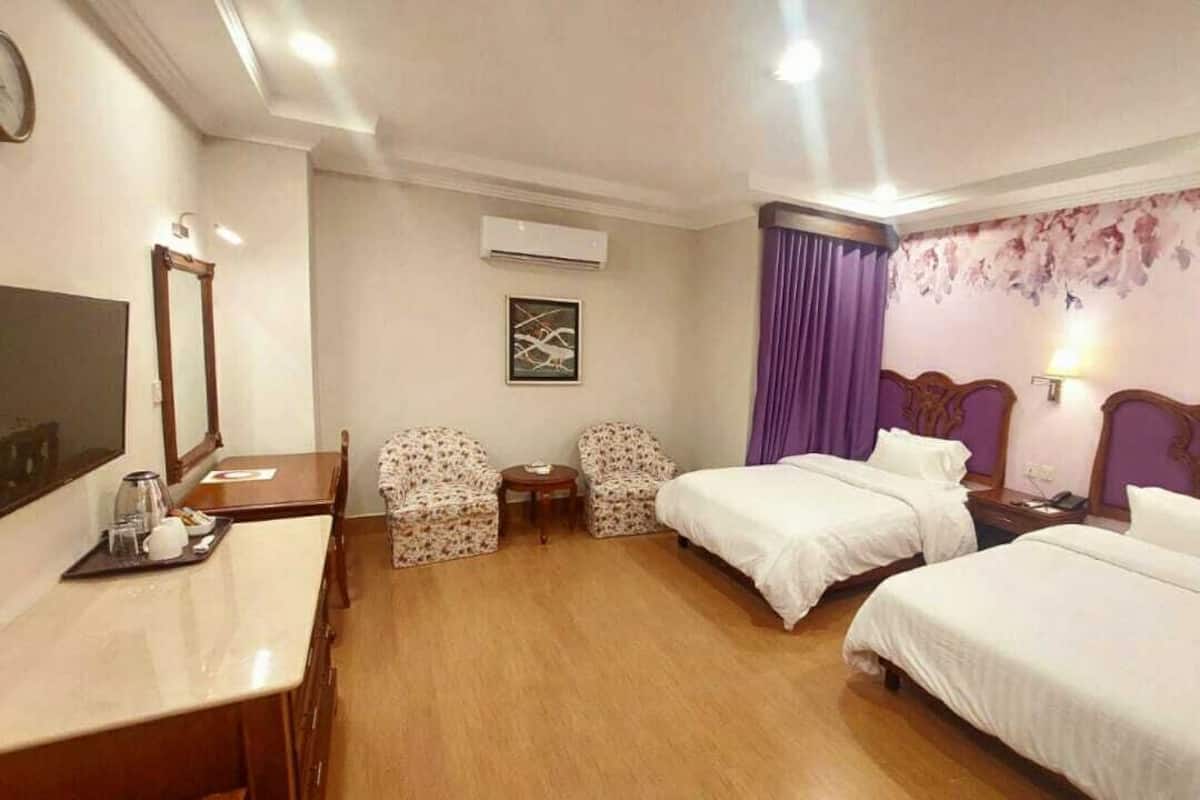 A hotel room with two beds, a desk with a chair, a small table, and a mirror.