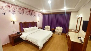 A hotel room with a large bed, two chairs, a desk with a mirror, and a purple curtain. - Hotel One Sargodha (Sargodha)