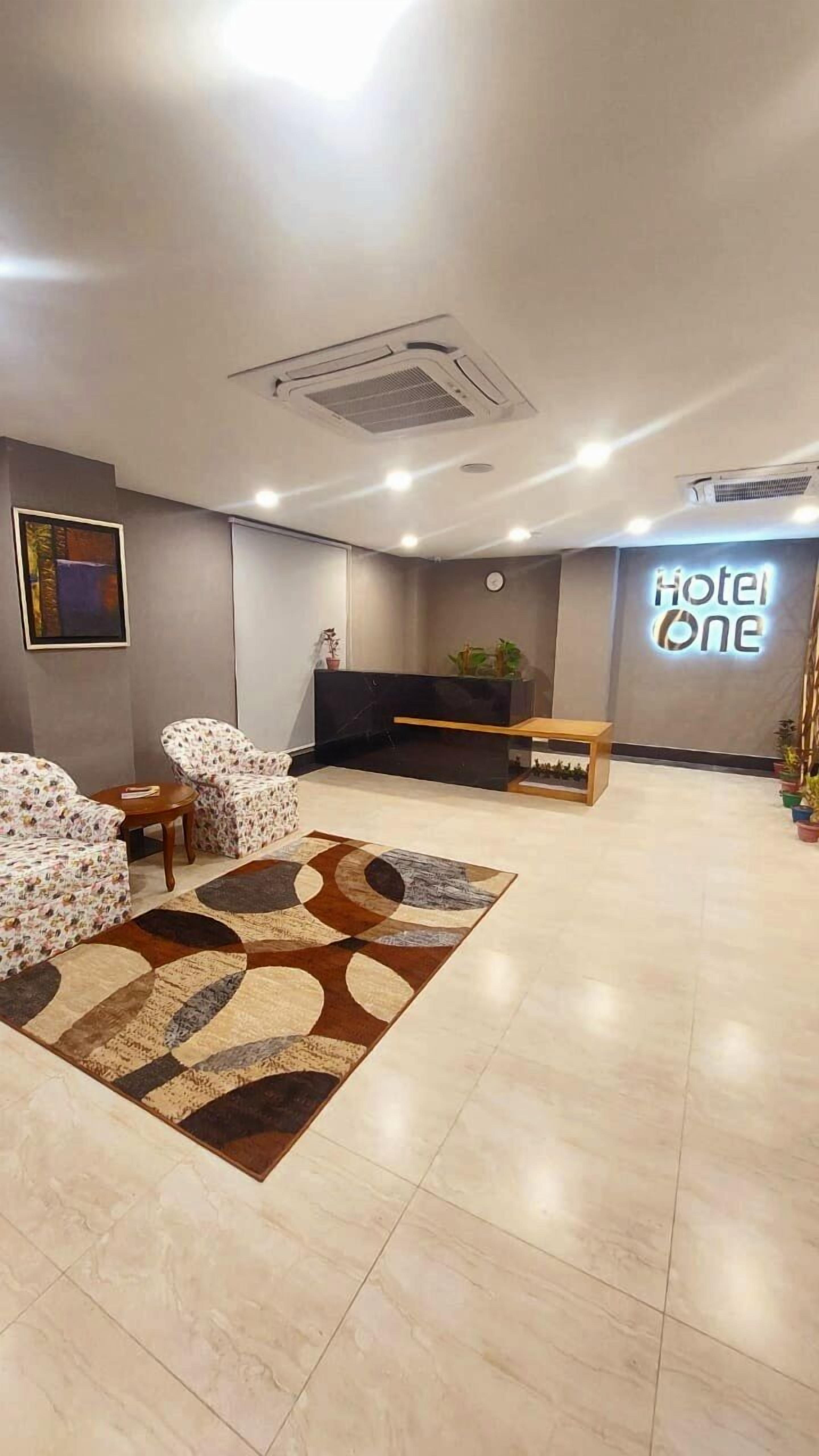 A hotel lobby with a reception desk, two patterned sofas, a coffee table, and a decorative rug.