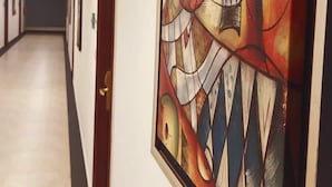 A hallway with a large abstract painting on the wall, a door on the left, and a long corridor with doors at the end. - Hotel One Sargodha (Sargodha)