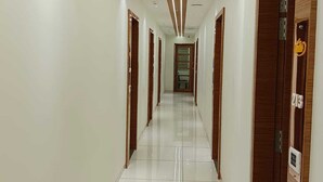 A long, narrow hallway with white walls and a shiny tiled floor. - Hotel Tulsi (Surat)