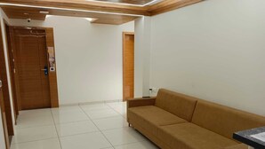 A modern room with a beige sofa, a wooden door, and a tiled floor. - Hotel Tulsi (Surat)