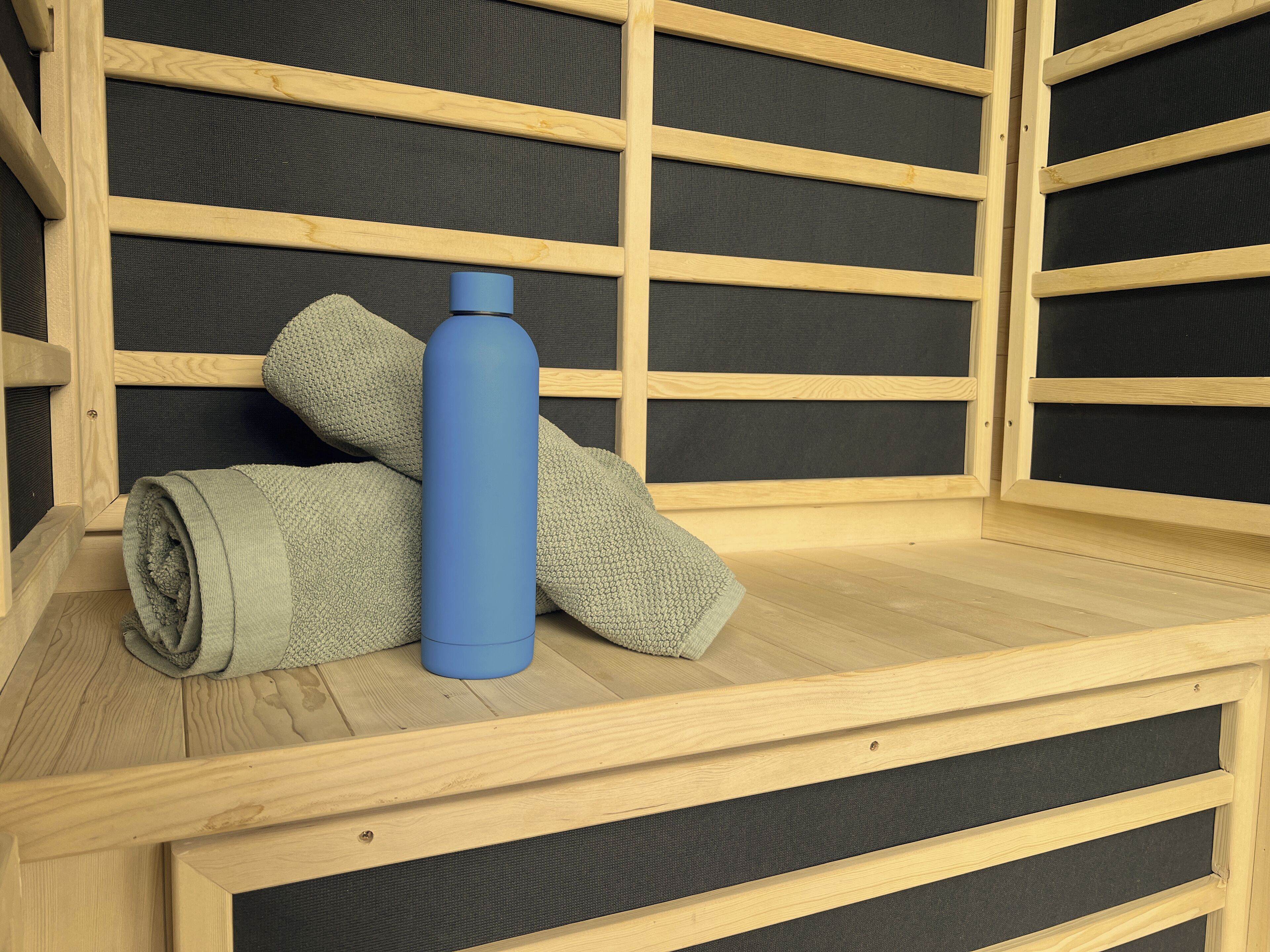 Un lit superposé en bois, avec une bouteille d’eau bleue et une serviette enroulée posées sur le lit.
